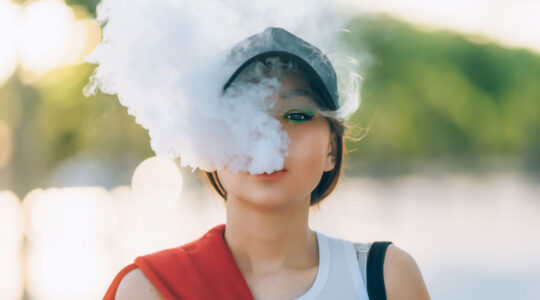 Jeune femme avec une casquette rejette la fumée de sa puff