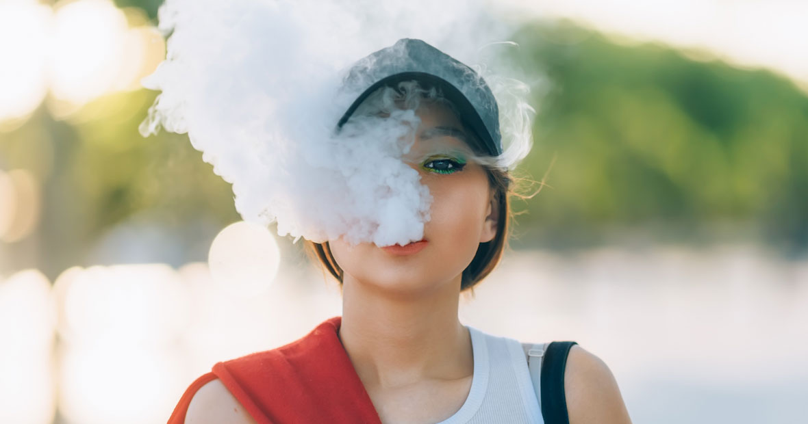 Jeune femme avec une casquette rejette la fumée de sa puff